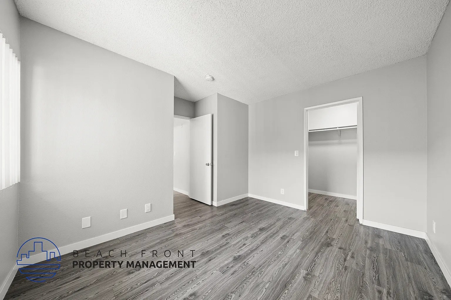 A room with wooden flooring and white walls, with a logo for Beach Front Property Management in the bottom left corner.